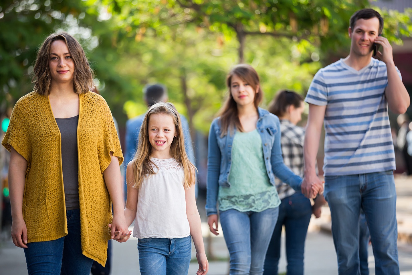 Eine vierköpfige Familie mit zwei Töchtern geht in einem Boulevard spazieren. Im Hintergrund das grün der Bäume einer Allee.