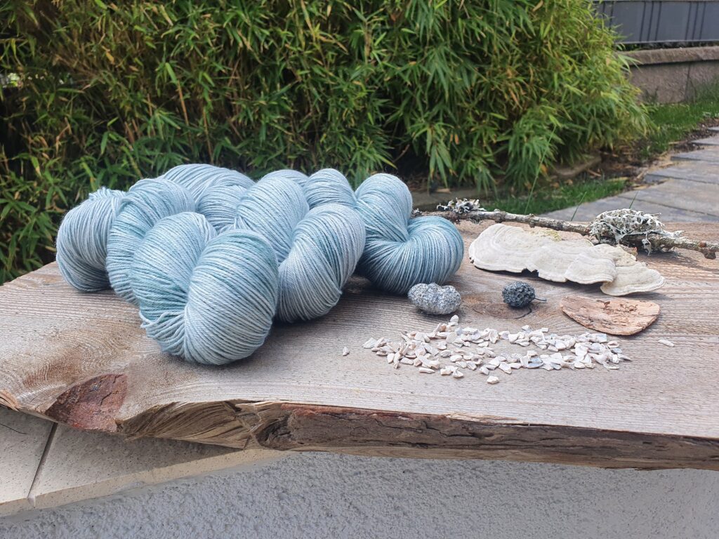 Hellblaue Wollzöpfe auf einer Baumscheibe drapieren.